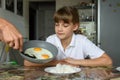 Mom cooked scrambled eggs for lunch and puts them from the pan on the daughter`s plate