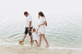 Mom, dad hugging daughter walking on the beach near lake. The concept of summer holiday. Mother`s, father`s, baby`s day. Family