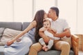 Mom and Dad kissing while the child looking at camera. Happy parents sitting home on couch in front of the window Royalty Free Stock Photo