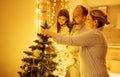 Mom, dad and little daughter decorate the Christmas tree at home. Young man, charming woman and their cute baby are getting ready