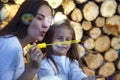 Mom and daughter blow bubbles on the background of firewood. Happy woman with child blow bubbles near stacked firewood. Royalty Free Stock Photo