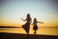 Mom with daughter in dresses are in a yoga pose on the lake at sunset. Leisure that strengthens the psychological health of the