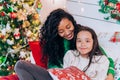 Mom and daughter hug sitting against Christmas tree