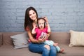 Mom and daughter listen to music in big headphones put on their head, sitting on the sofa. Holds the phone.