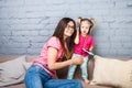 Mom and daughter listen to music in big headphones put on their head, sitting on the sofa. Holds the phone.