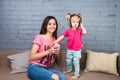 Mom and daughter listen to music in big headphones put on their head, sitting on the sofa. Holds the phone.