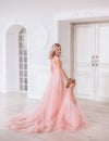 Mom and daughter in luxurious, pink dresses with a long train. Family clothes, identical dresses. The background is
