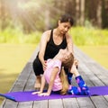 Mom and daughter perform gymnastic exercises on a sunny summer morning in the park on a wooden bridge