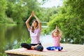 Mom and daughter perform a yoga exercise on the river bank on a warm summer day