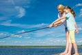 Mom and daughter are on the pier, against the blue sky and the lake, holding a fishing rod for fishing and point to the catch Royalty Free Stock Photo