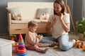 Mom and daughter playing together at a group lesson in the Montessori center, mommy and baby in casual clothes sitting on floor on