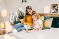 Mom and daughter are reading a book and smiling, sitting at home on the bed. New Year, Christmas, family, time together Royalty Free Stock Photo