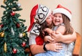 Mom and daughter in the red santa hat near Christmas tree. Mom kisses the child