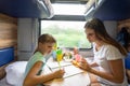 Mom and daughter sit at the table in the train and solve the puzzle in the children`s magazine