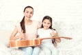 Mom and daughter are sitting on the couch at home. They have a guitar on their laps.