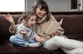 Young mother with her daughter are reading a book at home while sitting on the couch Royalty Free Stock Photo