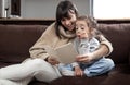 Young mother with her daughter are reading a book at home while sitting on the couch Royalty Free Stock Photo