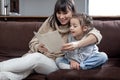 Young mother with her daughter are reading a book at home while sitting on the couch Royalty Free Stock Photo