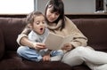 Young mother with her daughter are reading a book at home while sitting on the couch Royalty Free Stock Photo