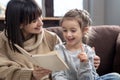 Young mother with her daughter are reading a book at home while sitting on the couch Royalty Free Stock Photo