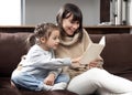 Young mother with her daughter are reading a book at home while sitting on the couch Royalty Free Stock Photo