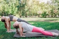 Mom and daughter are standing on hands and stretching their bodies. Girls are looking up. They are excercising outside