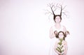 Mom and daughter in white dresses on a white background depict winter and spring, holding flowers and a twig with leaves.