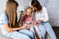 Mom and daughters sit on the bed in the bedroom and paint each other`s nails with nail Polish.