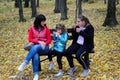 Mom with daughters are sitting on a bench in the autumn park.