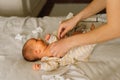 Mom dresses cute newborn little baby boy in a jumpsuit. Happy young mother playing with baby while changing his diaper on bed