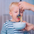 Mom feeding son. Boy cute baby eating breakfast. Child eat soup. Kid cute boy blue eyes sit at table with plate and food Royalty Free Stock Photo