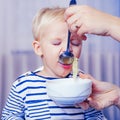 Mom feeding son. Boy cute baby eating breakfast. Child eat soup. Kid cute boy blue eyes sit at table with plate and food Royalty Free Stock Photo