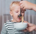 Mom feeding son. Boy cute baby eating breakfast. Child eat soup. Kid cute boy blue eyes sit at table with plate and food Royalty Free Stock Photo