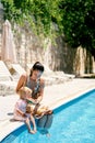 Mom feeds a little girl a watermelon sitting on the side of the pool with turquoise water Royalty Free Stock Photo