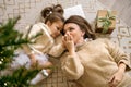 Mom gently kisses her daughter`s hands lying under the Christmas tree with gift box on the carpet on xmas Eve