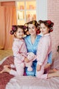 Mom and the girls are sitting on the bed in pink curlers and blue pajamas. Pajama party