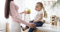 Mom giving fresh apple to little baby son, sitting on kitchentop