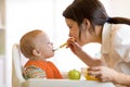 Mom giving fruit puree to her baby son on high chair. Royalty Free Stock Photo