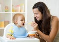 Mom giving homogenized food to her baby son on high chair in kitchen. Royalty Free Stock Photo