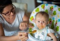 mom giving homogenized food to her daughter on high chair. Royalty Free Stock Photo