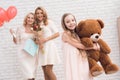 Mom, grandmother and girl are posing together near a light wall.