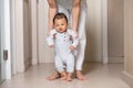 Mom helping and support baby learn to walk with love indoors at home. First steps of baby learning walk with family. Adorable