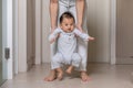 Mom helping and support baby learn to walk with love indoors at home. First steps of baby learning walk with family. Adorable