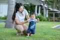 Mom helping and support baby learn to walk with love outdoors on grass. First steps of baby learning walk with family. Adorable