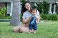 Mom helping and support baby learn to walk with love outdoors on grass. First steps of baby learning walk with family. Adorable