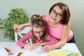 Mom helps the child write. Girl 6, 7 years old with glasses sitting at the table and writing in notebook