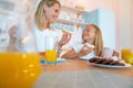 Mom and her daughter eat delicious donuts and have fun together. dressed in white t-shirts on colored kitchen background