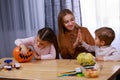 Mom and her kids are getting ready for Halloween. The girl paints a scary face on the pumpkin, while her mother slaps