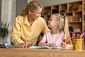 Mom and her little daughter sitting at desk and smiling to each other, mother helping her child with school homework Royalty Free Stock Photo