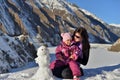 Mom and her little daughter in the winter sculpt a snowman in the mountains. Royalty Free Stock Photo